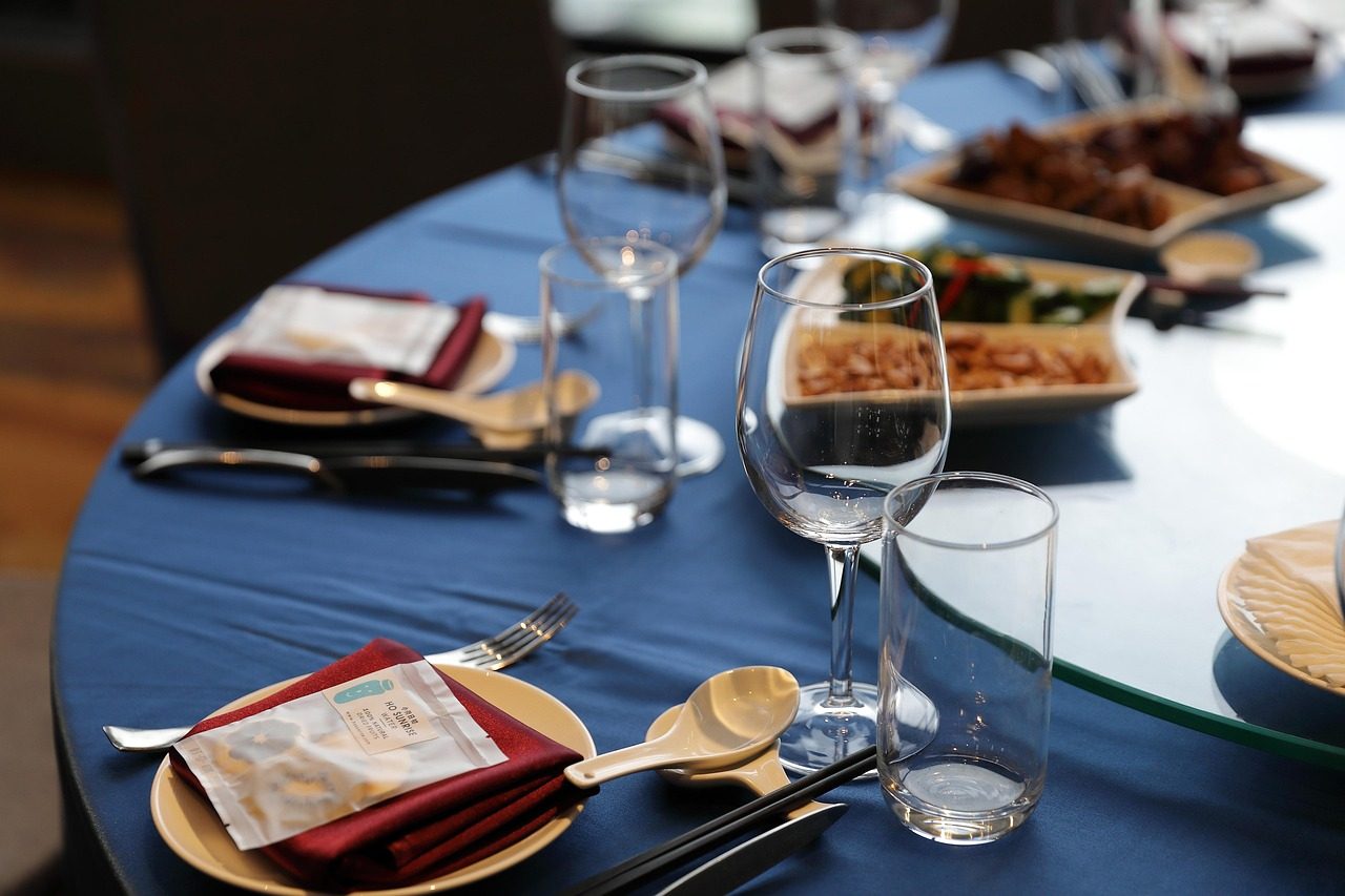 Eventmanagement Tischgedeck mit Gläsern, Besteck und mehreren Speisen auf einem blauen Tisch.