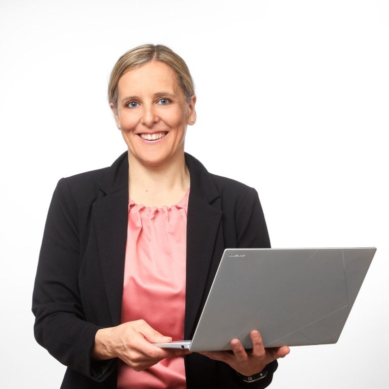 Eva Herz Eva Herz mit blonden Haaren, lächelnd, hält einen Laptop in der Hand. Sie trägt ein Blazer.
