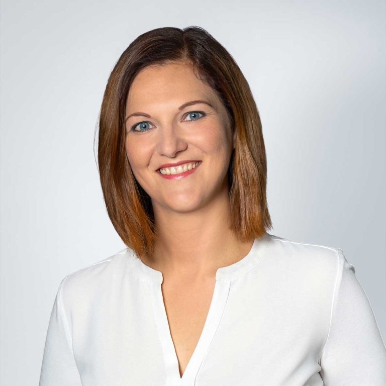 Daniela Anders Frau mit kurzen braunen Haaren, lächelt, trägt ein weißes Oberteil vor neutralem Hintergrund.