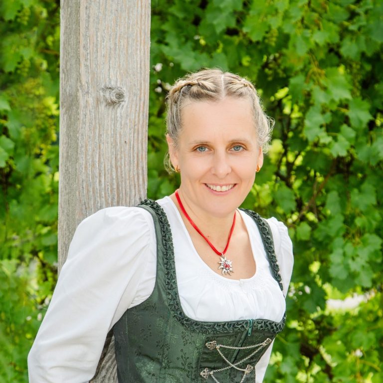 Beratung Frau in traditioneller Tracht vor grünem Hintergrund, lächelnd und mit Zöpfen.