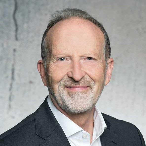 Dr. Christian Baumgartner Älterer Mann mit kurzen, grauen Haaren, lächelnd in einem Anzug vor neutralem Hintergrund.
