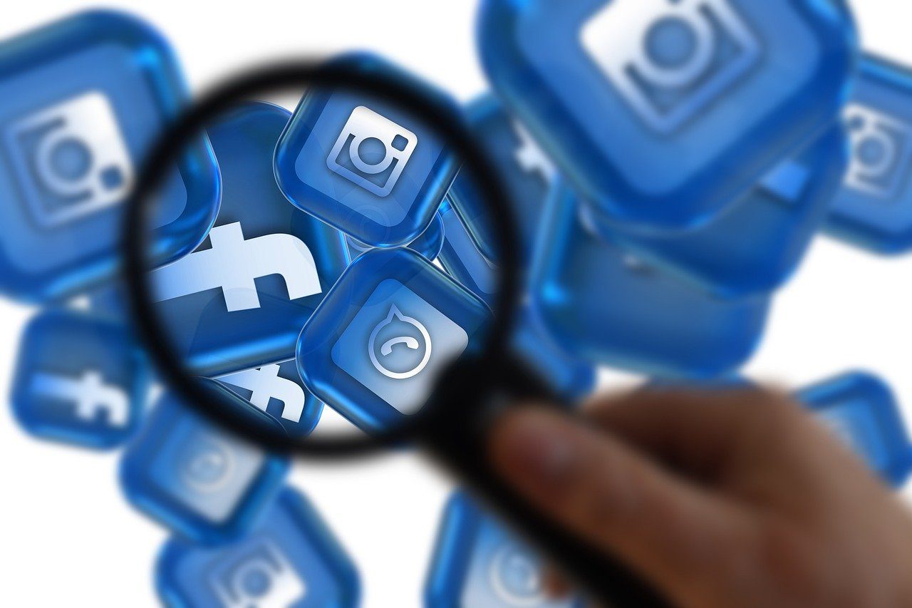 Social Media Vergrößerungsglas über blauen Social-Media-Symbolen, darunter Facebook und Instagram.